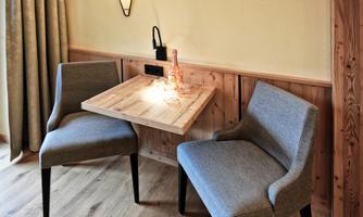 A cozy dining area with two gray chairs and a wood-colored table. A modern light hangs on the wall.