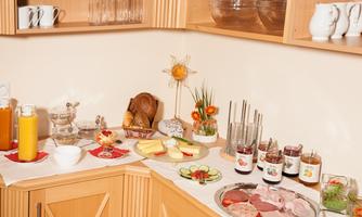 A rich breakfast buffet with various cold cuts, cheese, and jam. In addition, juice and fresh bread are available on a table.