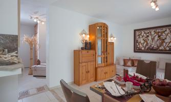 A bright living room with a wooden furniture piece and a dining table. The walls are in neutral colors and there is a cozy atmosphere.