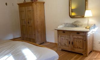 A cozy bedroom with a wooden bed and rustic furniture. There is a mirror and a lamp that create a warm atmosphere.