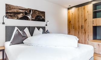 A modern bedroom with a large bed and decorative pillows. A stylish picture hangs on the wall, and the wooden wardrobe offers plenty of storage space.