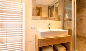 A modern bathroom with an elegant sink and a walk-in shower. Towels are neatly arranged on a shelf below.