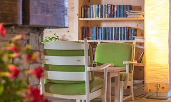 A cozy room with two green armchairs and a bookshelf in the background. A warm floor lamp provides an inviting light.