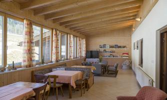 A bright room with large windows and a wooden beam ceiling. Tables and chairs invite you to sit and relax.