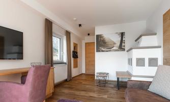 A modern living room with wooden flooring and a cozy sofa. A large picture hangs on the wall, and a television is integrated into the room design.