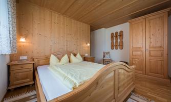 A cozy bedroom with wood paneling and a large bed. The decor is rustic with a wardrobe and nightstands made of wood.