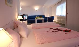A cozy room with a double bed and a sitting area. Rose petals adorn the bedspread, creating a romantic atmosphere.