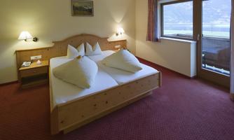 A cozy hotel room with a double bed and bright pillows. Large windows provide a view outside and the carpet creates a warm atmosphere.