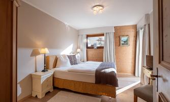 A cozy bedroom with a large bed and light wood decor. Daylight streams through the window, creating an inviting atmosphere.