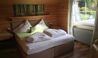 A cozy bedroom with a large bed and wooden paneling. The room has a window with a view to the outside and a natural light source.