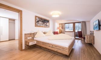 A cozy bedroom with a large bed and wooden details. Bright walls and a window create a friendly atmosphere.