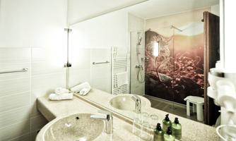A modern bathroom with a sink and a shower. The walls are brightly designed, and in the background, an artistic wallpaper can be seen.