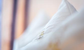 Soft, white pillows with fine embroidery. The background is blurred, creating a relaxed atmosphere.