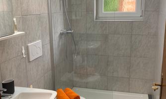 A modern bathroom with a shower cubicle and a sink. Orange towels are laid out on the shower shelf.