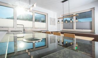 A modern kitchen with large windows and plenty of natural light. The shiny table reflects the surroundings and creates an inviting atmosphere.