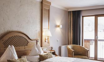 A cozy hotel room with two beds and a balcony. The warm colors and wood design create an inviting atmosphere.