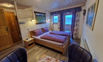 A cozy room with two single beds and wooden interior. There is a table with chairs and a window with a view outside.