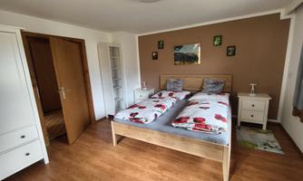 A cozy bedroom with a double bed and colorful bed covers. The walls are in soft colors, and there is a wardrobe as well as nightstands.