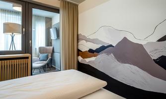 A modern room with a large window and a cozy seating area. The wall is decorated with a stylized mountain pattern.