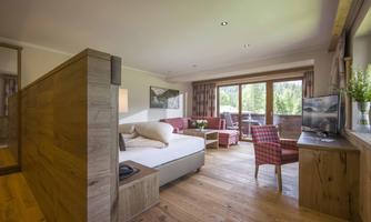 A modern room with wooden paneling and a cozy seating area. Large windows offer a view of nature and provide plenty of daylight.