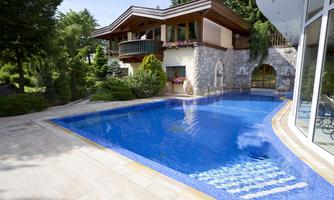 An elegant house with a beautiful garden and a blue pool. The surroundings are green and inviting.