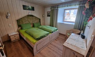A cozy bedroom with a double bed and fresh green bedding. The room is bright and features wooden walls as well as a window that lets in daylight.