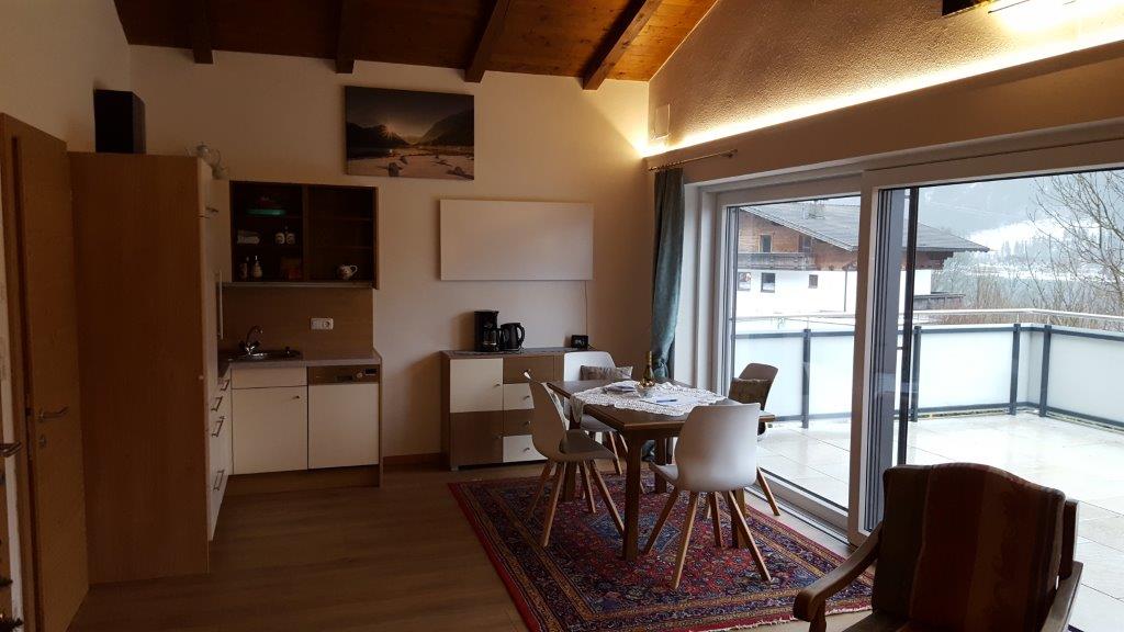 A modern living space with a kitchen and a dining area. Large windows provide a view of the terrace and the surrounding landscape.