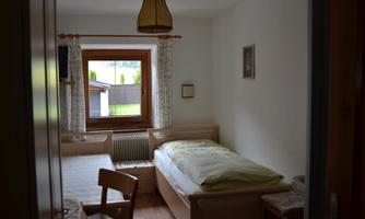A cozy bedroom with a single bed, a table, and a chair. The room has a window with a view outside and is simply but warmly furnished.