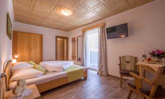 A cozy room with a double bed, a seating area, and a television. Large windows let in plenty of light and offer a view outside.