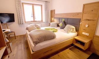 A cozy bedroom with two beds and wooden furniture. There is a TV and plenty of natural light coming through the window.