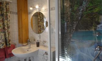 A bathroom with a round mirror and a modern shower. The walls are tiled, and there are colorful curtains.