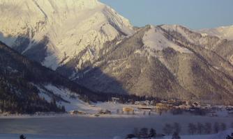 A snowy mountain panorama with majestic peaks. In the foreground, a frozen lake and a small village extend.