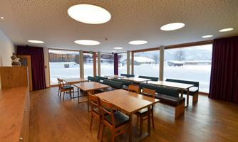 A modern furnished room with wooden chairs and tables. Large windows offer a view of the snowy landscape.