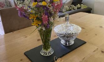 A beautiful table with a flower vase displaying fresh, colorful wildflowers. Next to it lies a lovingly wrapped gift on an elegant table coaster.