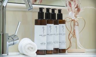 A stylish bathroom scene with four bottles of care products and a towel. The faucet and a decorative flower complete the elegant ambiance.