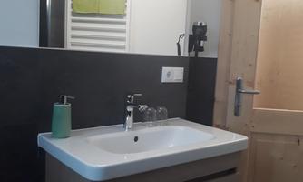 A modern bathroom with a sink and a wooden cabinet. On the wall hangs a towel holder and a green towel roll.