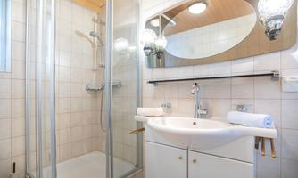 A modern bathroom with a shower cabin and an elegant sink. Bright tiles and a round mirror create a friendly atmosphere.