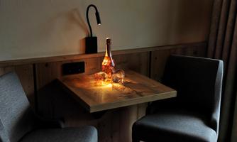 A small table with two gray chairs and a bottle of beverage, illuminated by soft light. The atmosphere is cozy and inviting.