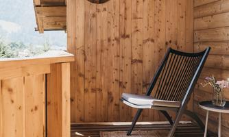 A beautiful balcony with wooden walls and a comfortable chair. On the floor lies a carpet and next to it stands a small table.
