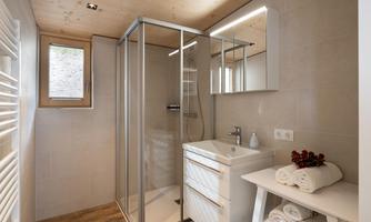 A modern bathroom with a glass shower and an elegant sink. Fresh towels are ready on a shelf.