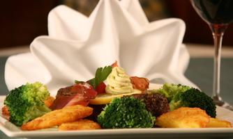 A beautifully arranged plate with vegetables and meat. In the background, there is a folded napkin and a glass of wine.