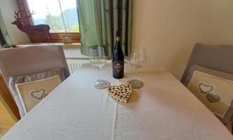 A table set with glasses and a bottle of wine. In the center lies a heart-shaped coaster, surrounded by a cozy ambiance.