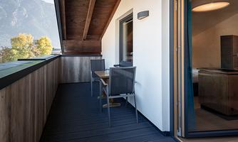 A modern balcony with two chairs and a table. In the background, the mountains can be seen and the room is open to the terrace.