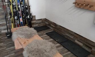 A ski storage room with a wooden bench and skins. Skis and a wardrobe for ski equipment hang on the wall.