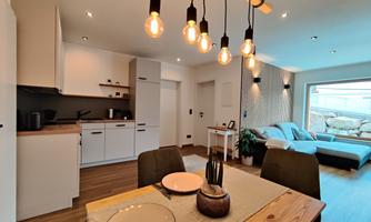 A modern kitchen with a dining area and a cozy living room.  
Bright lamps and elegant furniture create an inviting atmosphere.