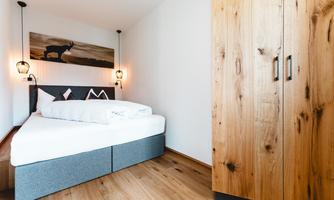 A modern bedroom with a large bed and a wooden wardrobe. The walls are light, and there is a decorative mural.