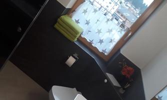 A modern bathroom with a window that offers a view of the surrounding mountains. On the windowsill, there are green towels and a flower.
