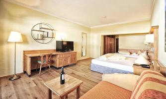 A cozy hotel room with wooden decor and a large bed. On the table, there is a bottle of wine, and there is a TV corner.