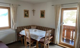 A cozy dining area with a table and chairs. Through the windows, you can see a balcony and the surrounding nature.