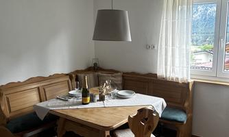 A cozy dining area with a wooden table and benches. The room has large windows that let in plenty of daylight.
